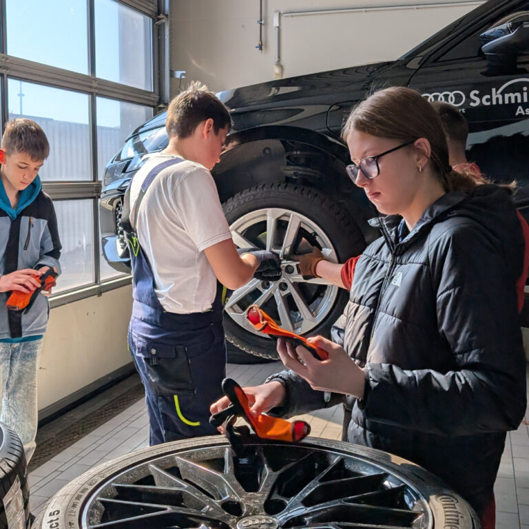 Auf dem Bild sind 3 Schüler*innen sowie ein Auzibi in der Audi Werkstatt zu sehen, wie sie dabei sind Radschraueben festzuziehen im Rahmen des Girls und Boys Day 2026